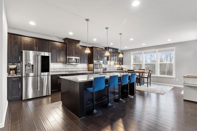 kitchen with decorative light fixtures, a kitchen island with sink, appliances with stainless steel finishes, and dark wood-type flooring