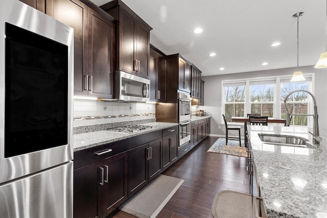 kitchen with sink, light stone counters, dark hardwood / wood-style floors, pendant lighting, and appliances with stainless steel finishes