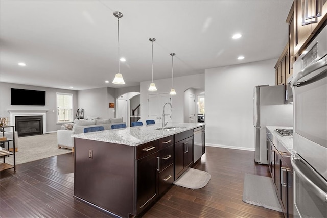 kitchen with dark brown cabinetry, sink, an island with sink, and decorative light fixtures