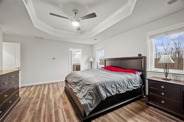 bedroom featuring ensuite bath, ceiling fan, a raised ceiling, crown molding, and wood-type flooring