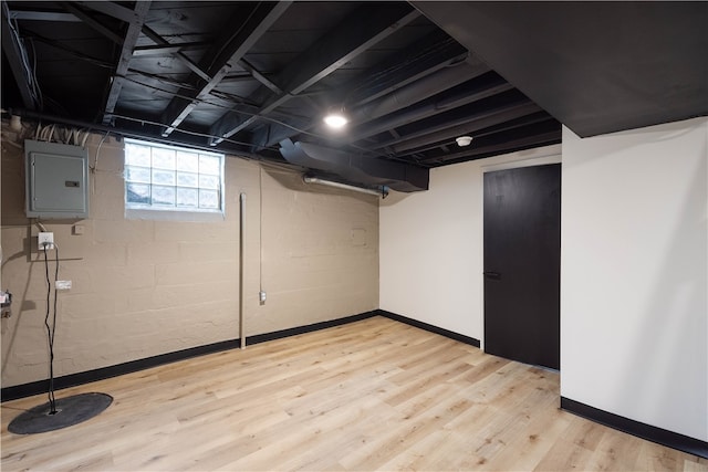 basement featuring electric panel and light hardwood / wood-style flooring