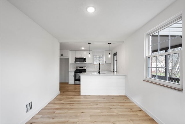 kitchen with white cabinetry, stainless steel appliances, tasteful backsplash, light hardwood / wood-style flooring, and pendant lighting