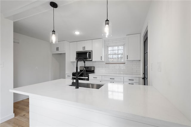 kitchen featuring appliances with stainless steel finishes, light wood-type flooring, sink, pendant lighting, and white cabinetry