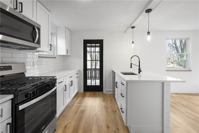 kitchen featuring stainless steel appliances, a healthy amount of sunlight, sink, decorative light fixtures, and white cabinetry