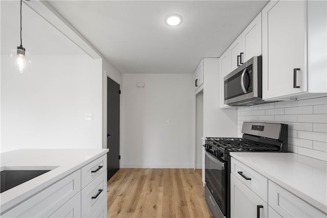 kitchen with pendant lighting, white cabinets, decorative backsplash, appliances with stainless steel finishes, and light hardwood / wood-style floors