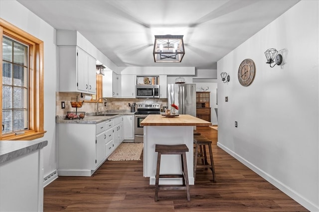 kitchen with wood counters, white cabinets, a kitchen breakfast bar, appliances with stainless steel finishes, and dark hardwood / wood-style flooring