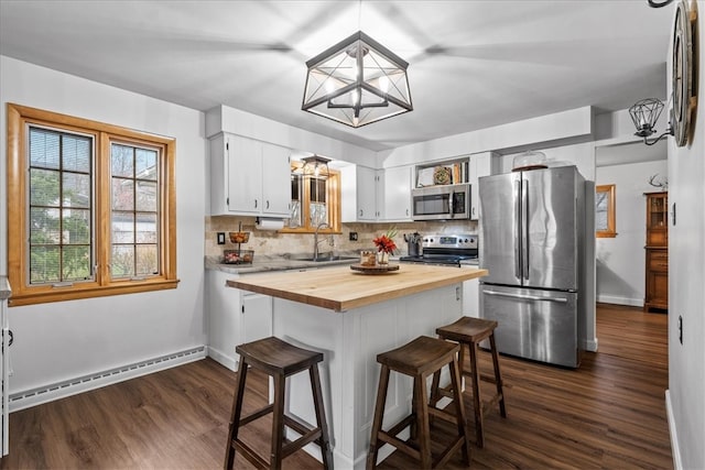 kitchen with stainless steel appliances, baseboard heating, a breakfast bar area, white cabinetry, and butcher block counters