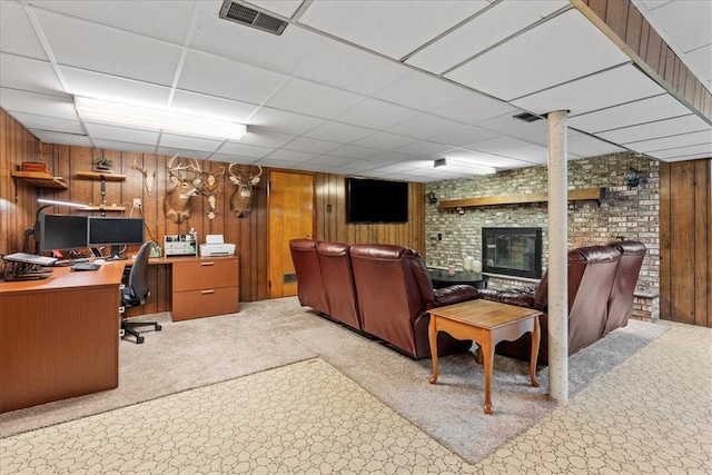 carpeted living room featuring wooden walls and a drop ceiling