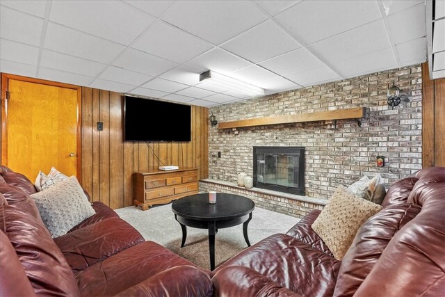 carpeted living room featuring a fireplace, wood walls, a drop ceiling, and brick wall