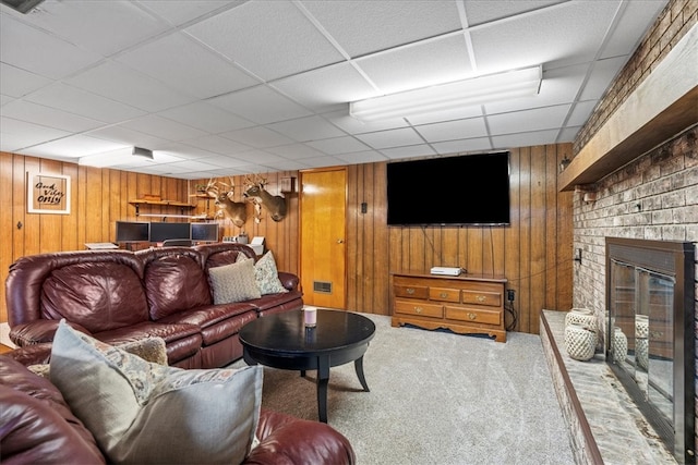 carpeted living room with a paneled ceiling, a brick fireplace, and wooden walls