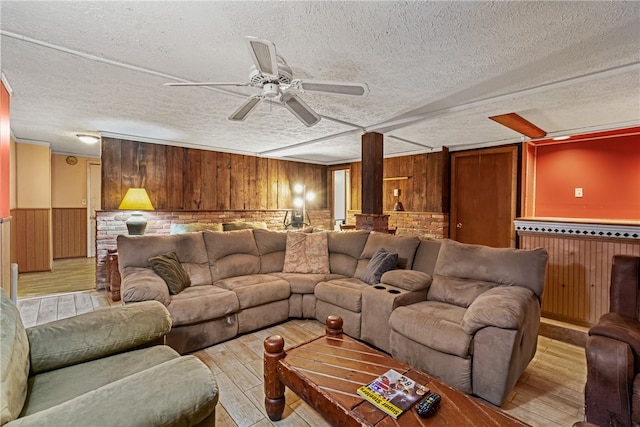 living room with a textured ceiling, light wood-type flooring, ceiling fan, and wood walls