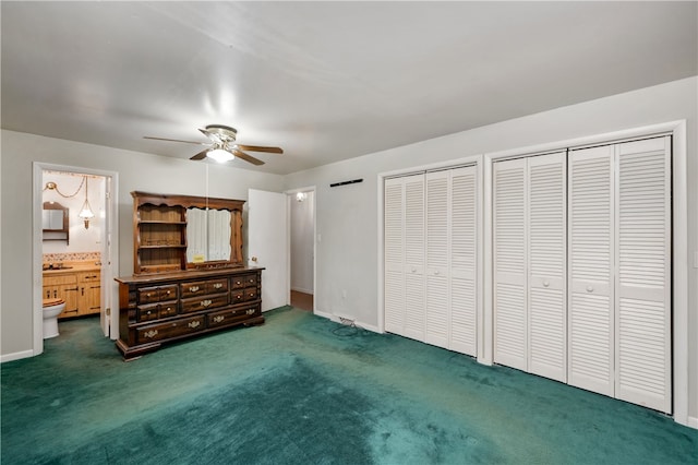 unfurnished bedroom with dark colored carpet, ceiling fan, multiple closets, and ensuite bath