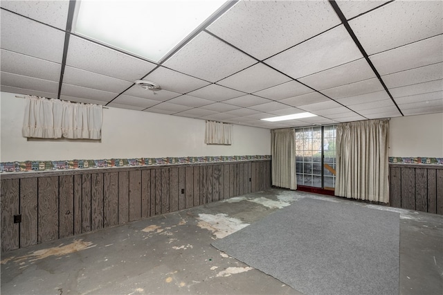 basement featuring a paneled ceiling and wood walls