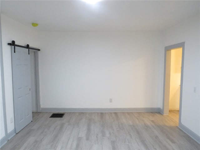 unfurnished bedroom featuring a barn door and light hardwood / wood-style floors