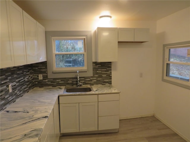 kitchen with white cabinets, decorative backsplash, light hardwood / wood-style floors, and sink