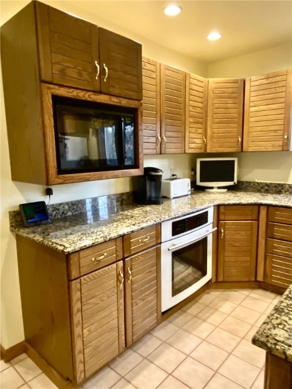 kitchen with stainless steel oven, light tile patterned floors, and stone countertops