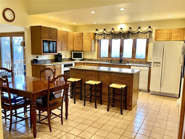 kitchen featuring white refrigerator with ice dispenser, a center island, stainless steel dishwasher, and stone counters