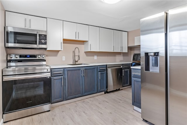 kitchen with blue cabinets, sink, light wood-type flooring, appliances with stainless steel finishes, and white cabinetry