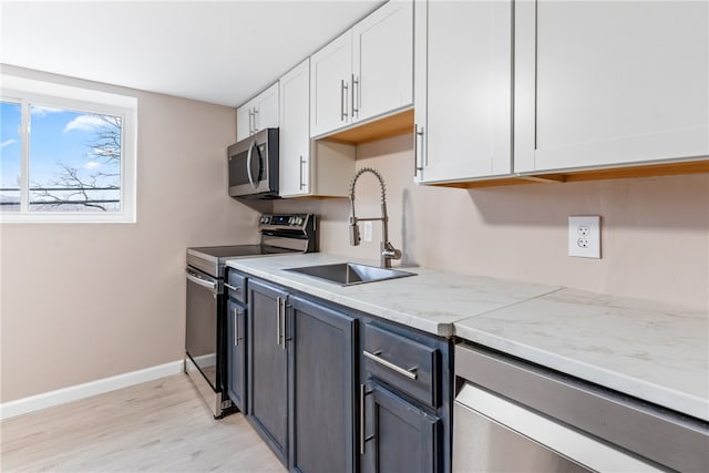 kitchen with sink, stainless steel appliances, light stone counters, light hardwood / wood-style flooring, and white cabinets