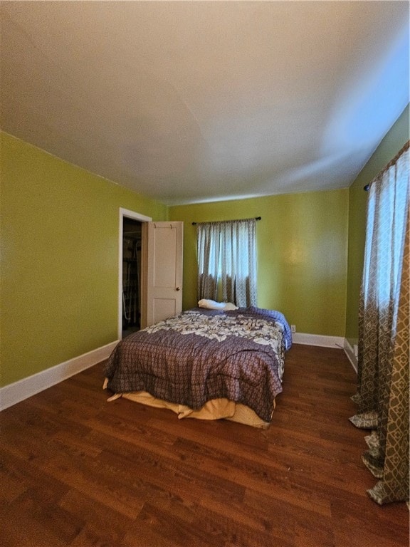 bedroom with vaulted ceiling, dark hardwood / wood-style flooring, a walk in closet, and multiple windows