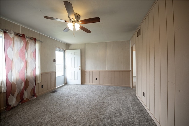 unfurnished room with light colored carpet, ceiling fan, and wooden walls