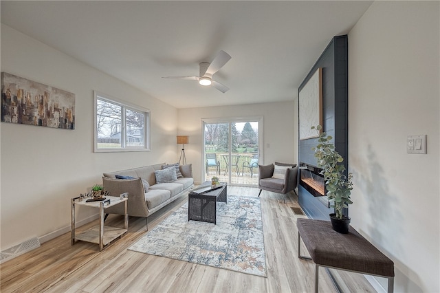 living room featuring ceiling fan, light wood-type flooring, and a large fireplace