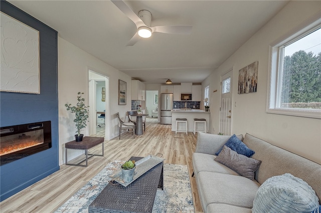 living room with light wood-type flooring, ceiling fan, and a fireplace