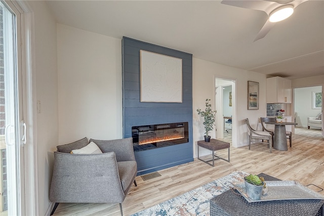 living room with light hardwood / wood-style floors, a large fireplace, and ceiling fan