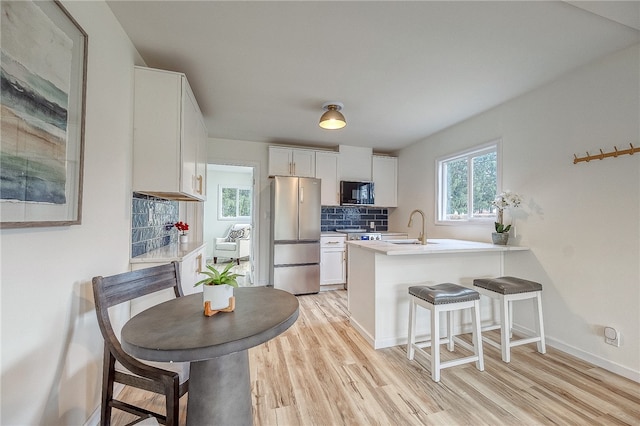 kitchen with white cabinetry, black microwave, backsplash, kitchen peninsula, and stainless steel refrigerator