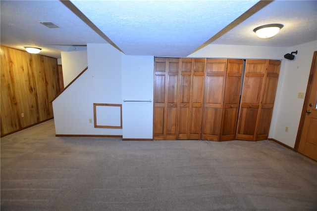 basement featuring light carpet, a textured ceiling, and wooden walls