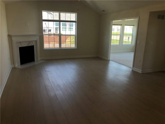 unfurnished living room with vaulted ceiling, a healthy amount of sunlight, wood-type flooring, and a premium fireplace