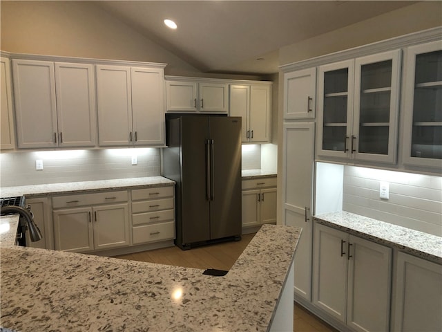 kitchen with vaulted ceiling, light stone countertops, tasteful backsplash, white cabinetry, and stainless steel refrigerator