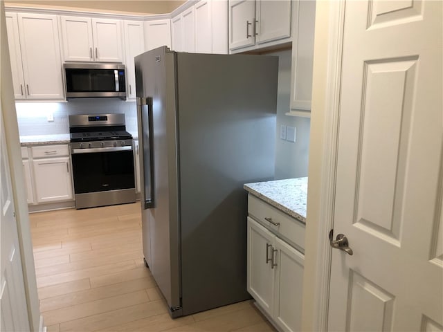 kitchen with tasteful backsplash, light stone counters, stainless steel appliances, white cabinets, and light hardwood / wood-style floors