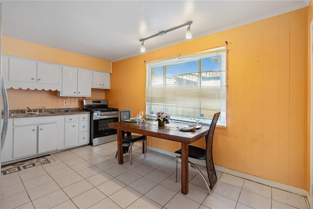 kitchen featuring stainless steel range with gas cooktop, white cabinets, light tile patterned flooring, and wood walls