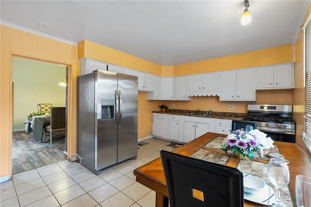 kitchen with appliances with stainless steel finishes, crown molding, sink, light tile patterned floors, and white cabinetry