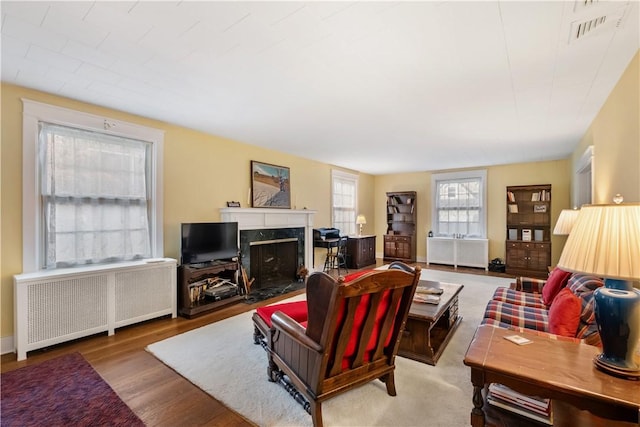 living room featuring a high end fireplace, radiator, visible vents, and wood finished floors