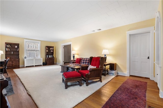 living area featuring radiator heating unit, wood finished floors, visible vents, and baseboards