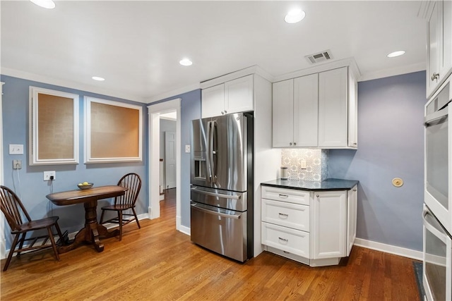 kitchen with light wood finished floors, visible vents, dark countertops, appliances with stainless steel finishes, and white cabinetry