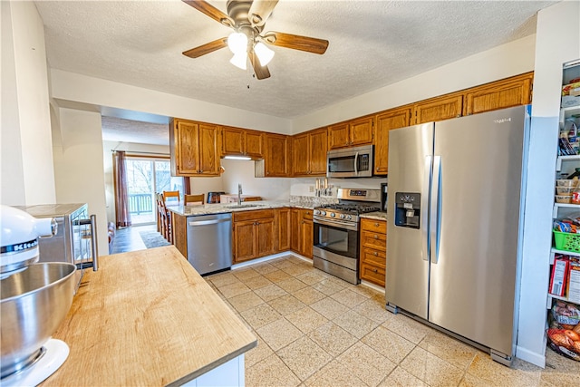 kitchen with ceiling fan, sink, a textured ceiling, and appliances with stainless steel finishes