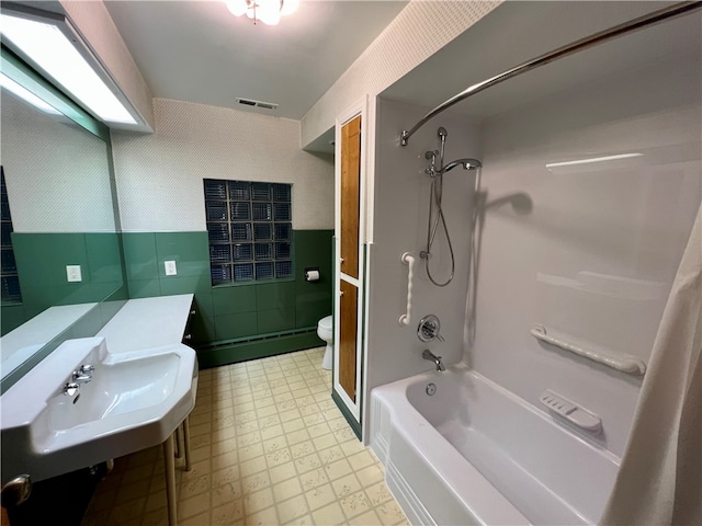 bathroom featuring tub / shower combination, toilet, and tile walls