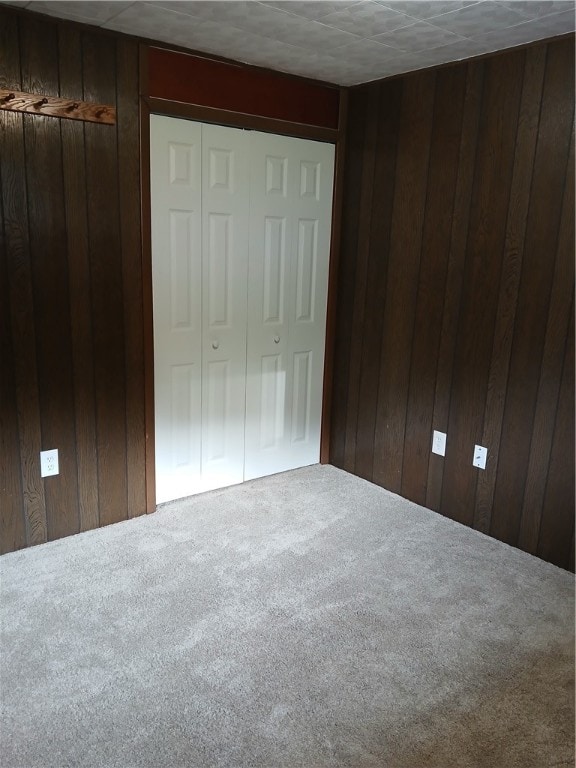 unfurnished bedroom with carpet flooring, wooden walls, and a closet