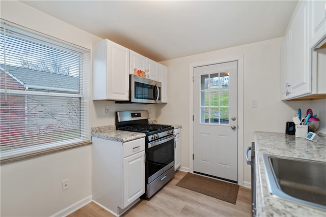 kitchen featuring white cabinets, sink, light stone countertops, light wood-type flooring, and appliances with stainless steel finishes