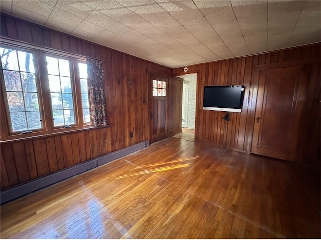 interior space with wood-type flooring, wooden walls, and a baseboard heating unit