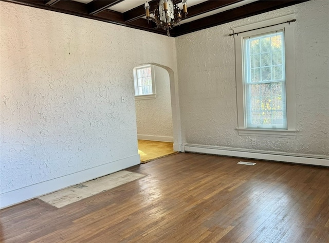 empty room featuring beam ceiling, wood-type flooring, a baseboard radiator, and a chandelier