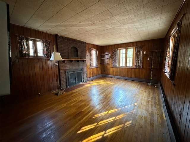 unfurnished living room with wood walls, wood-type flooring, and a brick fireplace