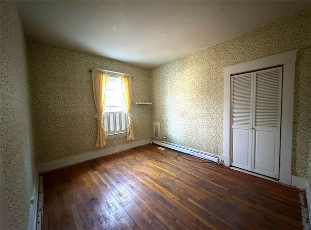 unfurnished bedroom with baseboard heating, a closet, and hardwood / wood-style floors