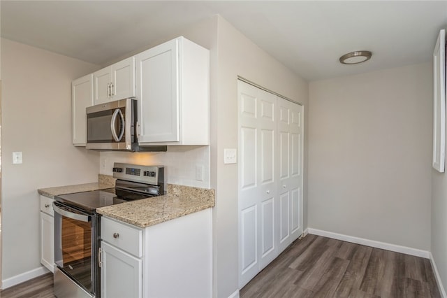 kitchen featuring appliances with stainless steel finishes, white cabinetry, dark wood-type flooring, and light stone counters