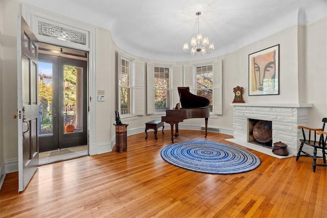 entrance foyer featuring a notable chandelier, a stone fireplace, light wood-type flooring, and french doors