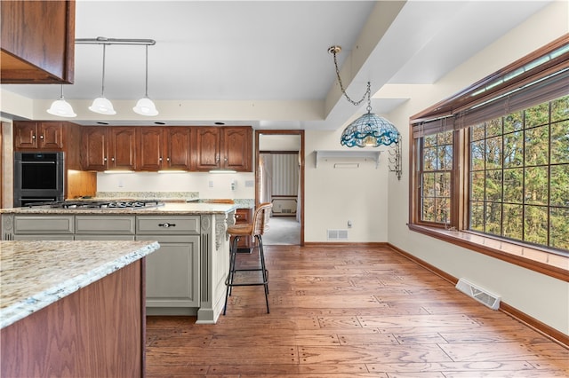 kitchen featuring a kitchen bar, light wood-type flooring, light stone counters, double oven, and decorative light fixtures