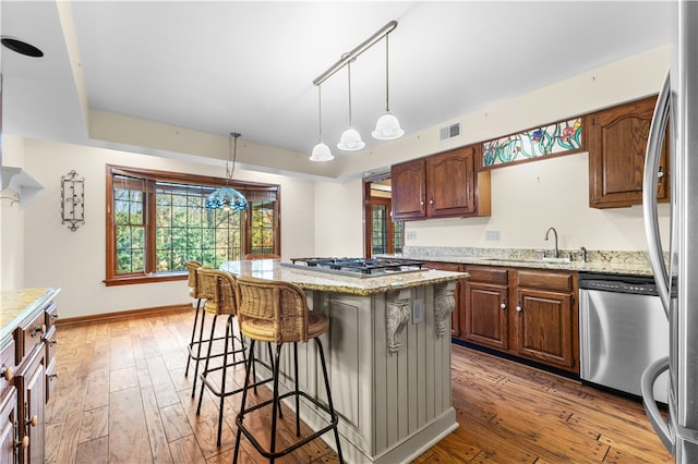 kitchen featuring appliances with stainless steel finishes, light stone counters, sink, hardwood / wood-style floors, and a kitchen island